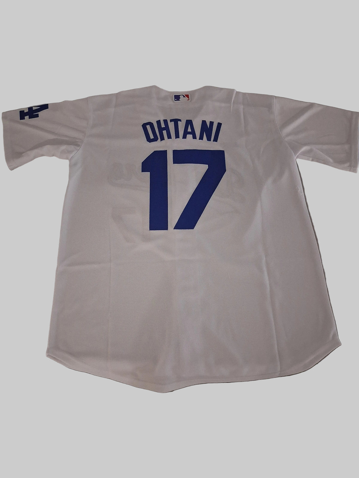 A white Los Angeles Dodgers jersey with 'OHTANI' and the number '17' in blue on the back, laid flat on a gray surface.